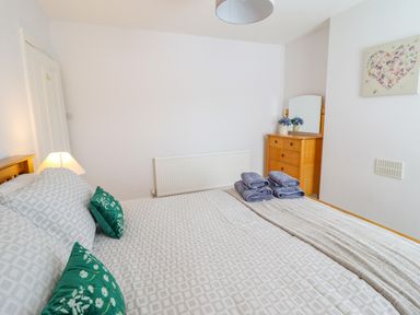 A bedroom with a bed with folded towels on it and a wooden dresser with a mirror at 24 Cadnant Park in Conwy