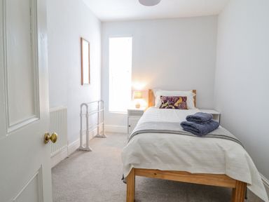 A small bedroom with a single wooden bed white bedding blue towels and a bedside table lamp at 24 Cadnant Park in Conwy