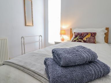 A bedroom with a single bed towels on the bed a bedside table with a lamp and a wall mirror at 24 Cadnant Park in Conwy