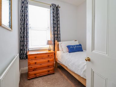 A small bedroom with a single bed a wooden chest of drawers a lamp and patterned curtains at 24 Cadnant Park Conwy