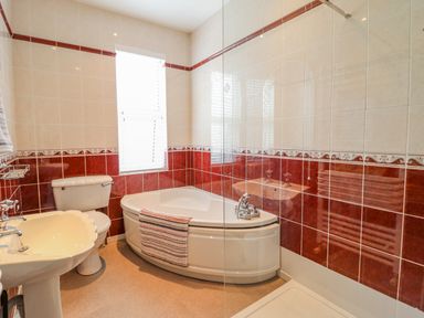 A bathroom with a corner bathtub a toilet and a sink with red and white tiles at 24 Cadnant Park in Conwy