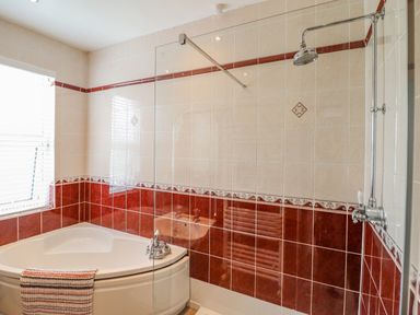 A bathroom with a corner bathtub a shower area with a glass partition and tiled walls at 24 Cadnant Park in Conwy