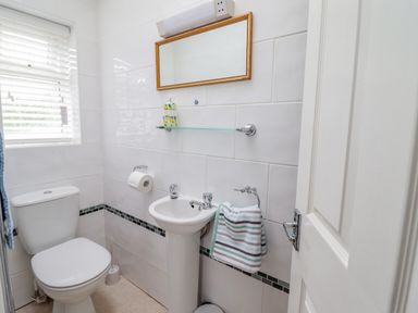 A small bathroom with a toilet, pedestal sink, mirror, towel, and window at 24 Cadnant Park Conwy