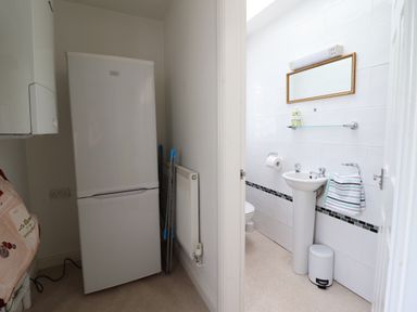 A utility area with a refrigerator and drying rack next to a bathroom with a sink mirror and towel at 24 Cadnant Park in Conwy