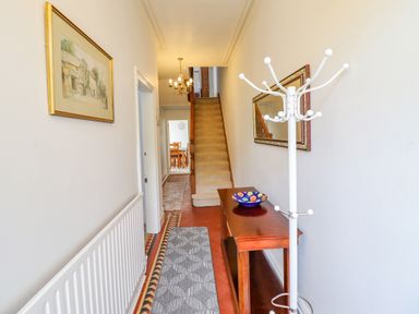 A hallway with a carpet runner a wooden table with a bowl a white coat rack and stairs leading up at 24 Cadnant Park in Conwy