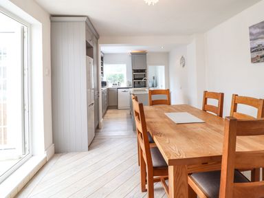 A dining area with a wooden table and chairs next to a kitchen with grey cabinets and appliances at 24 Cadnant Park in Conwy