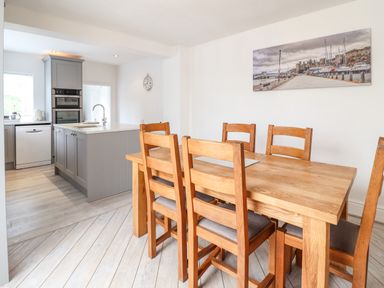 A dining area with a wooden table and six chairs next to a kitchen with a grey island and built-in ovens at 24 Cadnant Park in Conwy