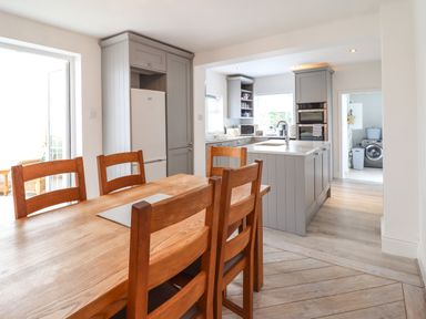 A kitchen and dining area with wooden table and chairs grey cabinets and a washing machine visible through an adjoining room at 24 Cadnant Park in Conwy