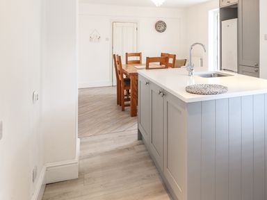 A kitchen with a gray island counter with a sink next to a wooden dining table with six chairs at 24 Cadnant Park in Conwy