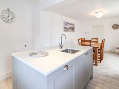 A kitchen island with a sink and faucet in front of a wooden dining table with chairs at 24 Cadnant Park in Conwy