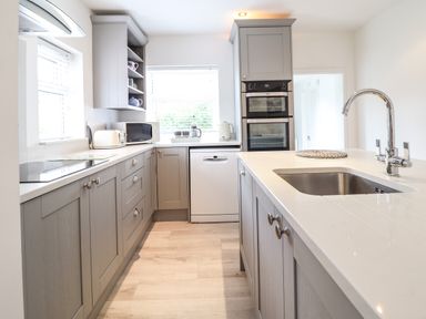 A kitchen with gray cabinets a white countertop a built-in oven a dishwasher a microwave a toaster and a sink with a faucet at 24 Cadnant Park in Conwy