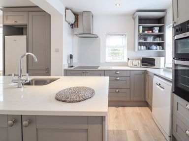 A kitchen with grey cabinets a white countertop a sink a microwave a toaster and an oven at 24 Cadnant Park in Conwy