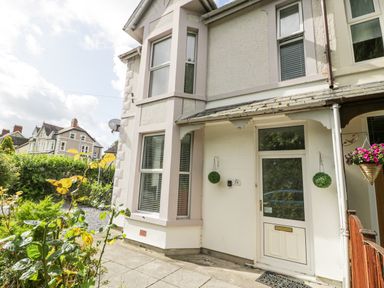 The front entrance of a white house with a door and windows surrounded by plants and neighboring houses at 24 Cadnant Park in Conwy