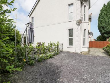 A side view of a white house with a gravel driveway and patio furniture with an umbrella at 24 Cadnant Park in Conwy
