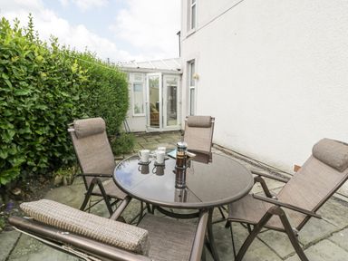 An outdoor patio with a glass table and four chairs near a white building at 24 Cadnant Park in Conwy
