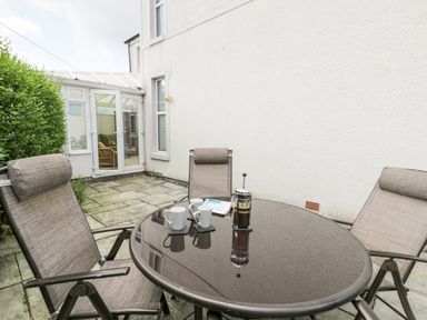 An outdoor patio with a glass table and three chairs and a coffee press with mugs at 24 Cadnant Park in Conwy