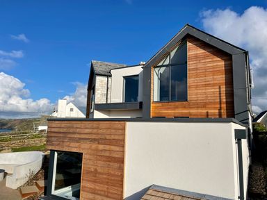 A modern house with wood and white exterior walls under a blue sky at The Old Coastguard Lookout in Port Isaac