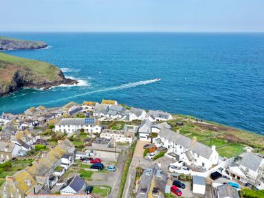 A coastal village with houses near the ocean and a boat leaving a trail in the water at The Old Coastguard Lookout in Port Isaac