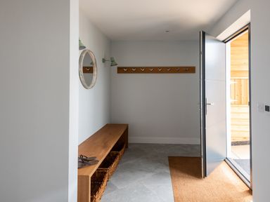 An entryway with a wooden bench with baskets underneath a round mirror and wall hooks next to an open door at The Old Coastguard Lookout in Port Isaac