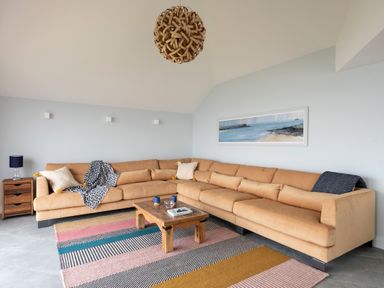 A living room with a large beige sectional sofa a wooden coffee table a colorful striped rug and a seascape painting on the wall at The Old Coastguard Lookout in Port Isaac