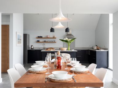 A dining table set with white bowls glasses and cutlery in front of a kitchen with black cabinets and shelves at The Old Coastguard Lookout in Port Isaac