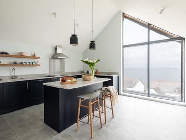 A kitchen with a central island stools pendant lights and large window with sea view at The Old Coastguard Lookout in Port Isaac