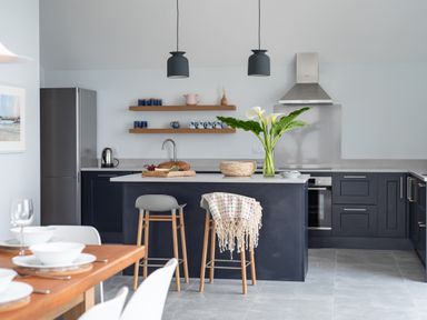 A modern kitchen with a central island two stools pendant lights and a dining table at The Old Coastguard Lookout in Port Isaac