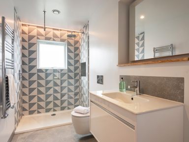 A bathroom with a walk-in shower featuring patterned tiles a toilet and a sink with a mirror at The Old Coastguard Lookout in Port Isaac