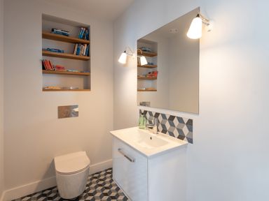 A bathroom with a toilet sink mirror wall lights and built in shelves with books at The Old Coastguard Lookout in Port Isaac
