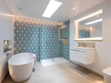 A bathroom with a bathtub a glass shower enclosure a patterned tile wall a white vanity with mirror at The Old Coastguard Lookout in Port Isaac