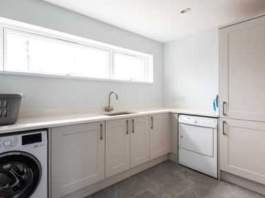 A laundry room with a washing machine dryer sink and cabinets at The Old Coastguard Lookout in Port Isaac
