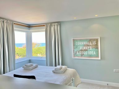 A bedroom with a bed and folded towels near corner windows and a framed sign on the wall at The Old Coastguard Lookout in Port Isaac