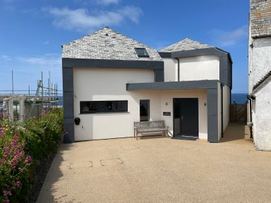 A modern two story house with a bench outside and flowers on the side at The Old Coastguard Lookout in Port Isaac