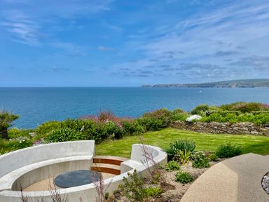 An outdoor seating area with a circular concrete bench and a round table overlooking the ocean at The Old Coastguard Lookout in Port Isaac