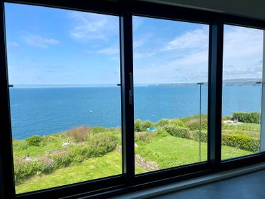 A view of the ocean and green garden through large glass sliding doors at The Old Coastguard Lookout in Port Isaac