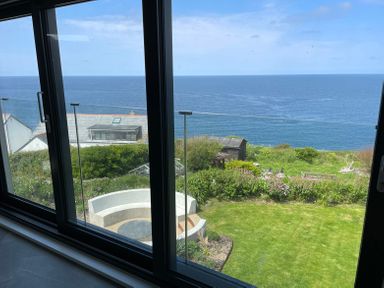 A garden with a curved white bench and grass overlooking the sea at The Old Coastguard Lookout in Port Isaac