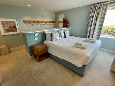 A bedroom with a bed a bedside table a window with curtains and a wall-mounted coat rack at The Old Coastguard Lookout in Port Isaac