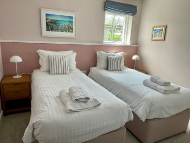 A bedroom with two single beds each with white bedding striped pillows and bedside tables with lamps at The Old Coastguard Lookout in Port Isaac