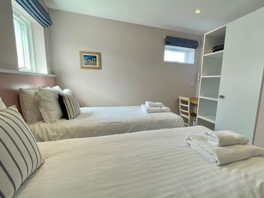 A bedroom with two single beds towels on beds a chair a wooden desk and open shelving at The Old Coastguard Lookout in Port Isaac
