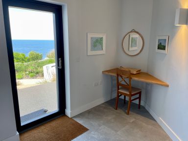 A corner desk with a chair and circular mirror next to a door with sea views at The Old Coastguard Lookout in Port Isaac
