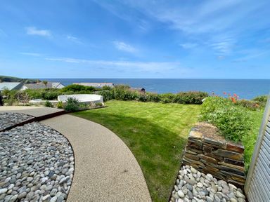 An outdoor garden with a circular stone seating area grass lawn and ocean view at The Old Coastguard Lookout in Port Isaac