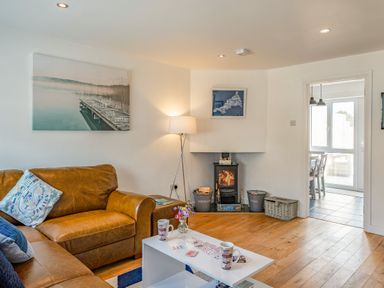A living room with a brown leather sofa a white coffee table a wood burning stove and a floor lamp at Shrimper's Cottage in Tredrizzick near St Minver