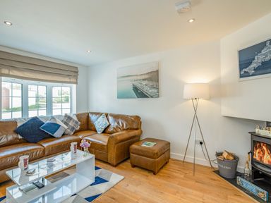 A living room with a brown leather corner sofa and cushions a white coffee table wooden floor and a fireplace with a standing lamp at Shrimper's Cottage in Tredrizzick near St Minver