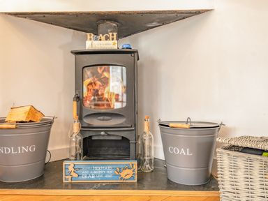 A wood burning stove with buckets labelled kindling and coal and decorative signs at Shrimper's Cottage in Tredrizzick near St Minver