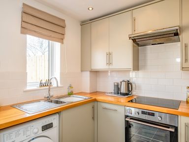 A kitchen with a sink, washing machine, electric stove, kettle, and cabinets at Shrimper's Cottage in Tredrizzick near St Minver
