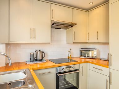 A kitchen with wooden countertops a sink an electric stove oven a toaster kettle and cabinets at Shrimper's Cottage in Tredrizzick near St Minver