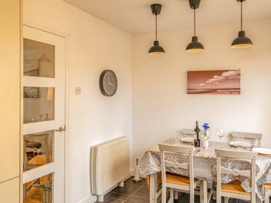 A dining room with a table set for four under three ceiling lamps at Shrimper's Cottage in Tredrizzick near St Minver