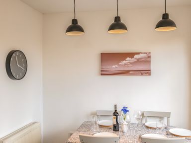 A dining table set with plates glasses a wine bottle and flowers under three pendant lights at Shrimper's Cottage Tredrizzick near St Minver