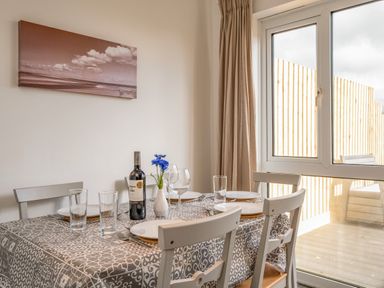 A dining table set with plates glasses wine bottle and flowers next to a window at Shrimper's Cottage in Tredrizzick near St Minver