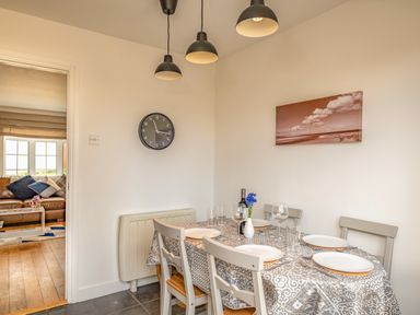 A dining room with a table set for four and a painting on the wall at Shrimper's Cottage in Tredrizzick near St Minver